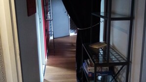 A narrow hallway with a bookshelf on the right, a red door at the end, and a patterned wall on the left. - Waterfront Apartment in Garennes-sur-Eure at Le Havre de Paix - Sleeps 3–4  (Neuilly)