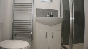 A bathroom with a toilet, a sink, a mirror, and a shower. - En Suite Rooms at the Rose and Thistle (Berwick-upon-Tweed)