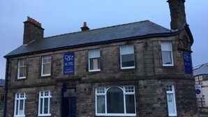 A two-story stone building with a dark roof, a central entrance with a blue door, and multiple windows. - En Suite Rooms at the Rose and Thistle (Berwick-upon-Tweed)