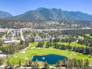 A golf course with a pond, surrounded by residential buildings and mountains. - The Sable Bright Side | Pool | Hot Tub | Top Floor (Radium Hot Springs)