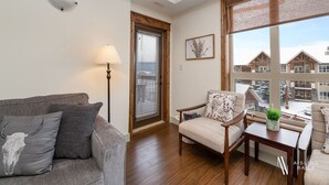 Ein Wohnzimmer mit grauem Sofa, einem Holzstuhl, einem Tisch und einem Fenster mit Jalousien.