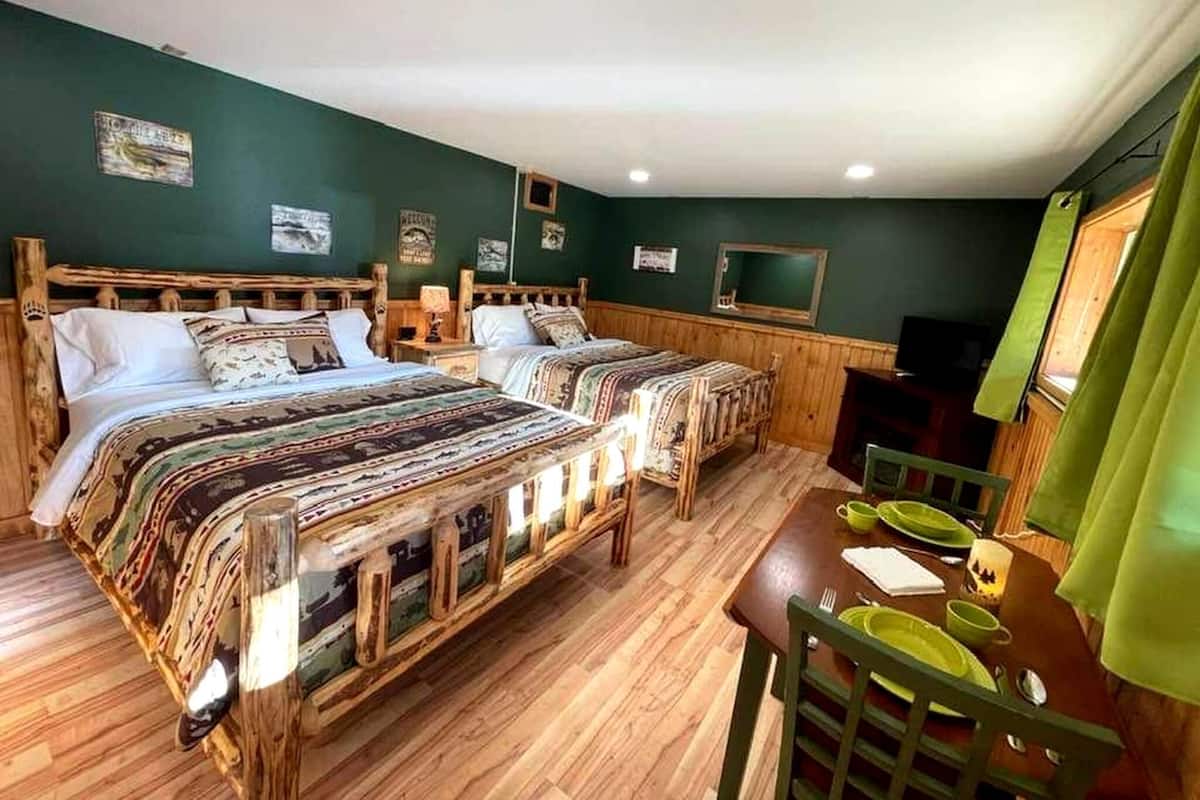 A room with two wooden beds, a dining table with chairs, and a television.