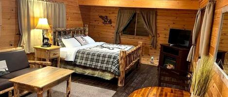 A wooden cabin interior with a bed, a sofa, a table, a TV, and a fireplace.