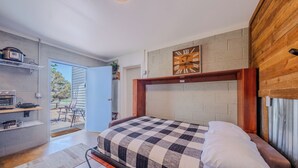 Una camera da letto con copriletto a quadretti, una testiera in legno, una sveglia a parete e vista sull'esterno.