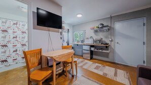 Un ambiente compatto con zona pranzo, cucina e TV a parete.