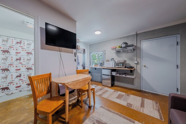 Un espacio habitable compacto con comedor, cocina y televisor montado en la pared.