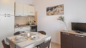 A modern kitchen with white cabinets, a dining table set with plates and candles, and a flat-screen TV on a cabinet. - Appartamenti Le Fontane con piscina (Villasimius)