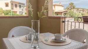 A balcony with a table set for two, a vase with flowers, and a view of buildings in the background. - Appartamenti Le Fontane con piscina (Villasimius)