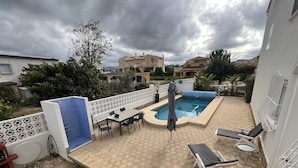 A backyard with a swimming pool, a covered patio table, lounge chairs, and a grassy area. - Vacation home in Oliva on the Costa Blanca, 10 minutes' walk from the sea. (Oliva Playa)