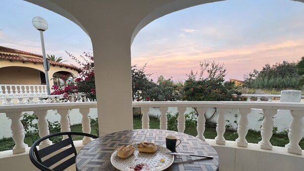A round table with a plate of food and a cup, set on a balcony with a railing and a view of a building and trees. - Vacation home in Oliva on the Costa Blanca, 10 minutes' walk from the sea. (Oliva Playa)