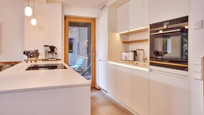A modern kitchen with white cabinetry, a built-in oven, and a coffee machine. - WunderSchön - cosy holiday flat with modern design and alpine charm (Garmisch-Partenkirchen)