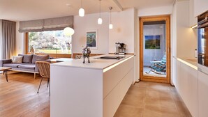 A modern kitchen with a central island, a dining area with a sofa and chairs, and a view of the outdoors through large windows. - WunderSchön - cosy holiday flat with modern design and alpine charm (Garmisch-Partenkirchen)