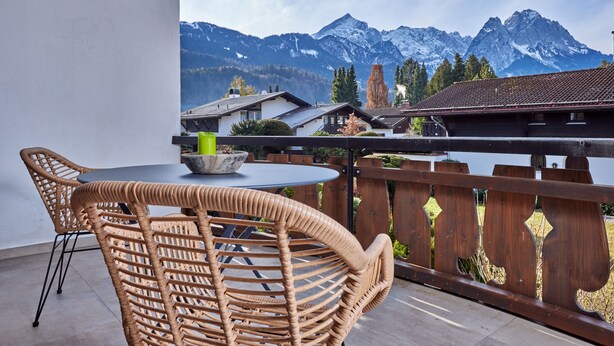 A balcony with wicker chairs and a table, overlooking a mountainous landscape. - WunderSchön - cosy holiday flat with modern design and alpine charm (Garmisch-Partenkirchen)