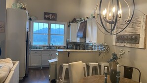 Une cuisine dotée d’une grande fenêtre, de meubles blancs et d’une table à manger avec des chaises, ainsi que d’un lustre.