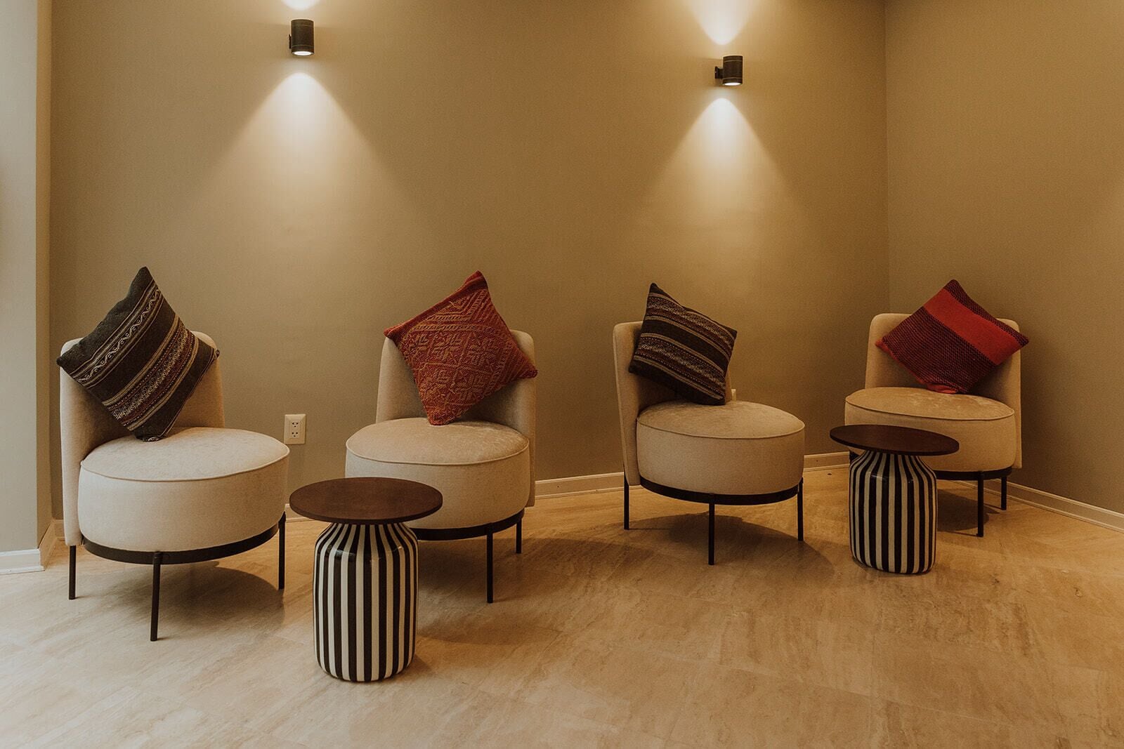 A room with four chairs and two small tables, each with a different patterned cushion.
