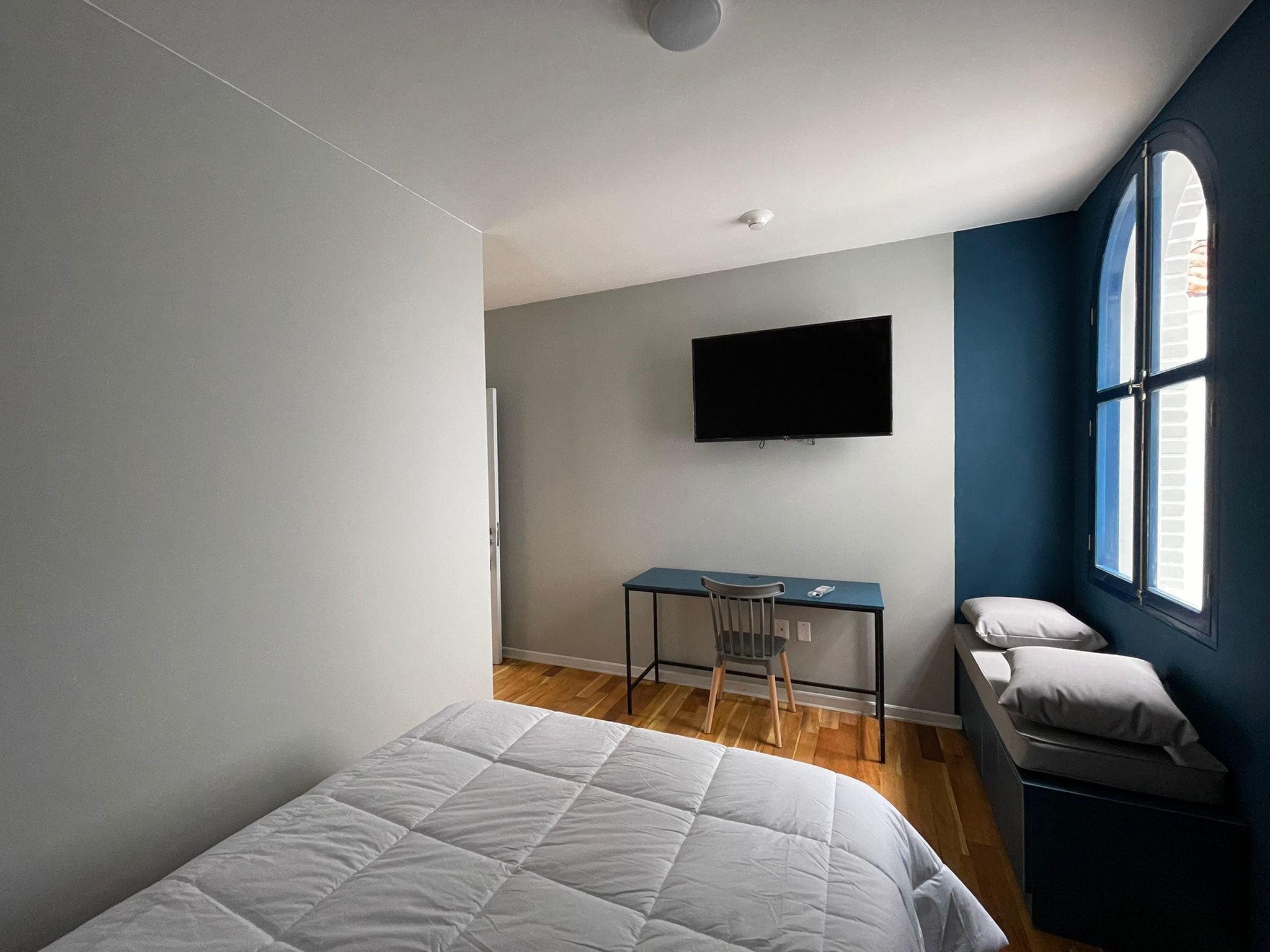 Een slaapkamer met een bed, een bureau, een stoel, een televisie en een raam.