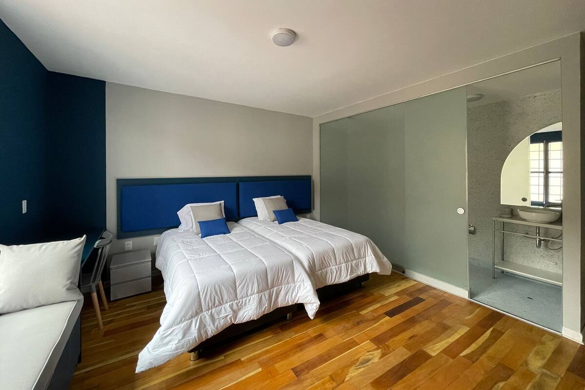 Un dormitorio moderno con una cama grande, una mesita de noche y un baño integrado con espejo y lavamanos.