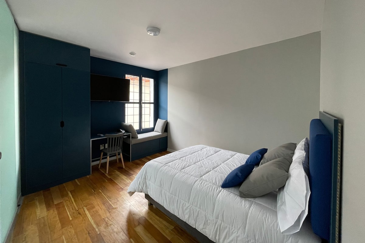 Un dormitorio con cama, escritorio y ventana.