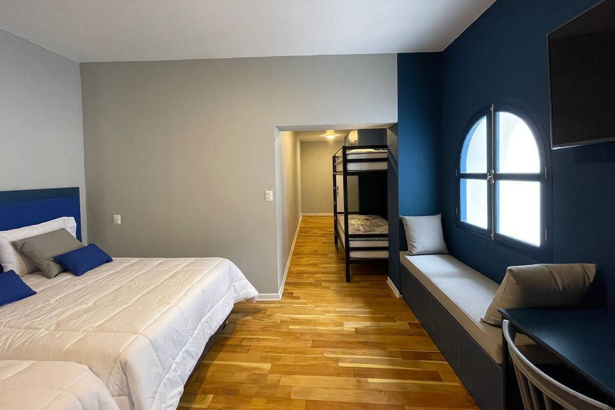 Una habitación de hotel con literas, un sofá, un televisor y un ventanal grande.