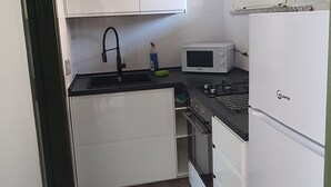 Et lille køkken med hvide skabe, en sort bordplade, en mikroovn, en vask og en ovn.