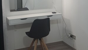 Et værelse med et hvidt skrivebord, en sort stol, et fladskærms-tv monteret på væggen og en aircondition oven over skrivebordet.