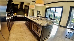 A modern kitchen with dark cabinetry, a granite countertop, and a large island. - Luxury Water Front Villa Freeport Bahamas (Freeport)