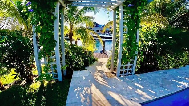 A garden pathway leading to a pool area with a pergola and lush greenery. - Luxury Water Front Villa Freeport Bahamas (Freeport)