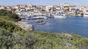 A coastal town with a marina, buildings with red roofs, and rocky terrain. - Capo Falcone Charming Apartments (Stintino)