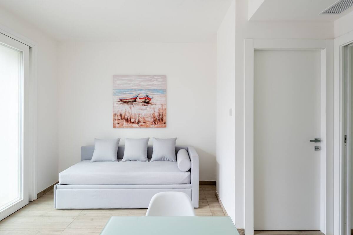 A modern living room with a sofa, a painting of boats on water, and a door.