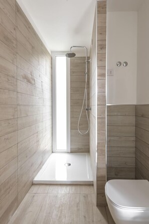 A modern bathroom with a shower, toilet, and a window providing natural light. - Capo Falcone Charming Apartments (Stintino)