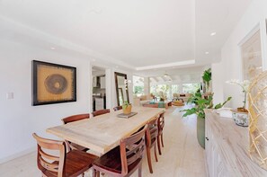 Un comedor amplio con una mesa y sillas de madera, un cuadro abstracto grande y vistas a la cocina y la sala de estar.