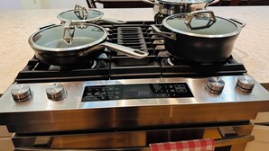 A stainless steel stove with four pots and pans, a digital control panel, and a dining table with chairs in the background. - Discover tranquility near Calvert Cliffs  (Saint Leonard)