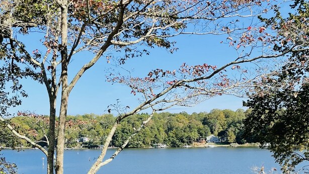 A wooden deck with chairs and tables overlooking a lake, surrounded by trees and a clear sky. - Discover tranquility near Calvert Cliffs  (Saint Leonard)