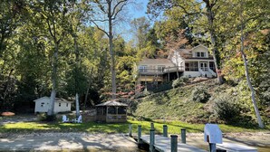 A two-story house with a porch and a small deck, surrounded by dense trees and a grassy area. - Discover tranquility near Calvert Cliffs  (Saint Leonard)