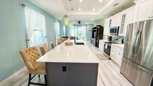Une cuisine moderne dotée d’un îlot central, d’appareils électroménagers en acier inoxydable et d’un coin repas agrémenté d’une chaise capitonnée.