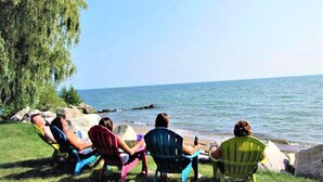 A group of people sitting on colorful Adirondack chairs by a lake. - Private Waterfront Belle Point Shores Cottages (Leamington)
