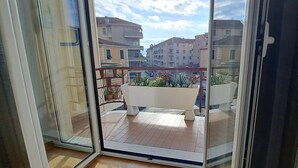 A balcony with a view of surrounding buildings, a potted plant, and a white bench. - Garibaldi 5: two-room apartment with sea view, bright, central, 2 large terraces (Sanremo)