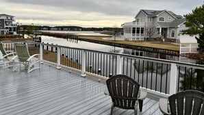 Eine Terrasse mit Stühlen, die auf ruhiges Wasser blickt, ein Haus mit Veranda und ein klarer Himmel.