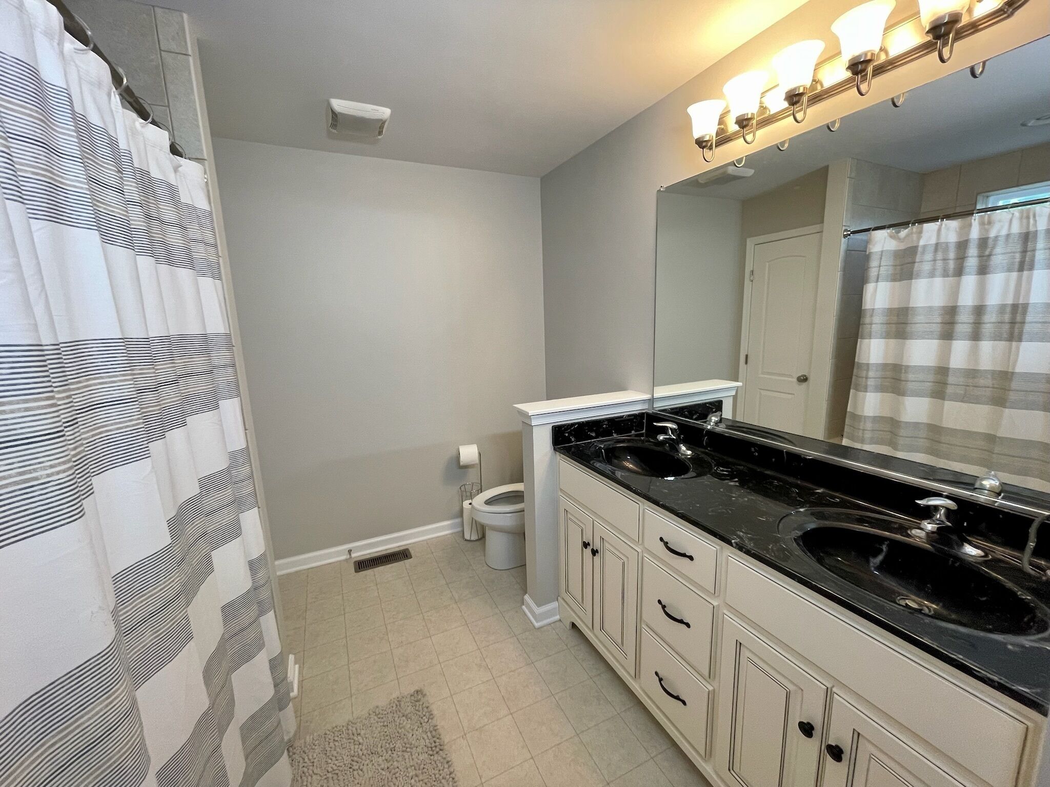 A bathroom with a black sink, white cabinets, a mirror, and a shower curtain.