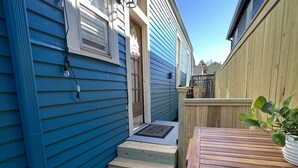 A wooden deck with a table and steps leading to a house with blue siding and a wooden fence. - Welcome to the JazzNest!   (New Orleans)