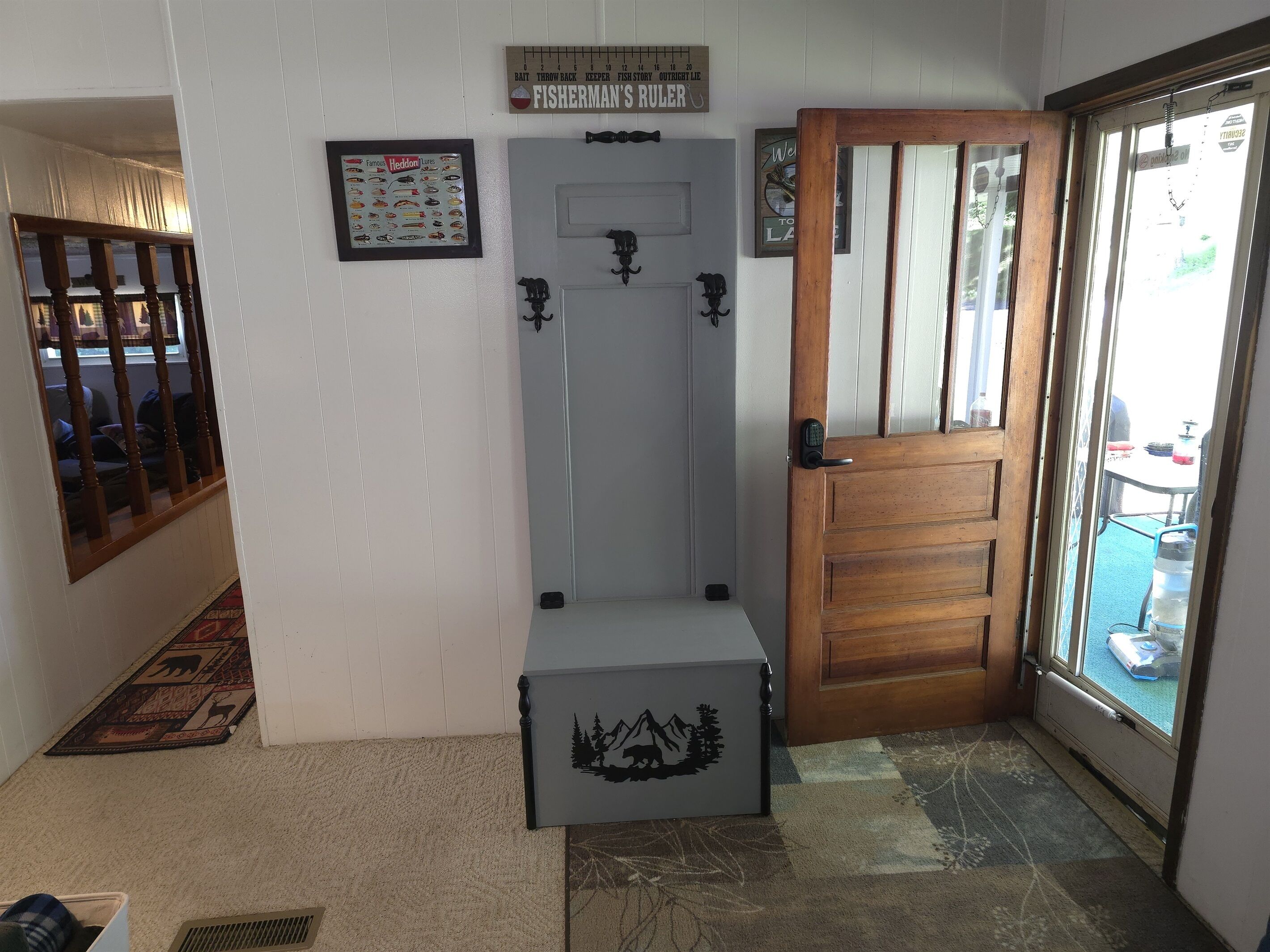 A hallway with a wooden door, a white wall with a fish-themed poster, a wooden bench, and a small table with a water dispenser.