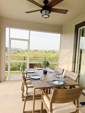 Varanda com mesa posta para refeições, ventilador de teto e vista para uma paisagem verde.