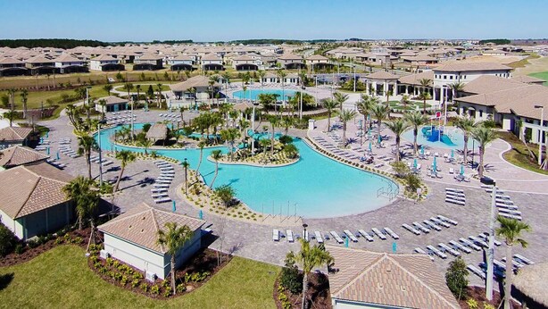 A resort with a large central pool, sun loungers, and a well-maintained lawn.