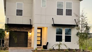 A modern two-story house with a garage, a front door, and a small garden area.