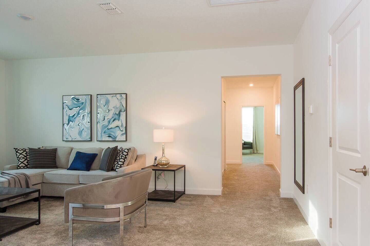 A living room with a sectional sofa, a small round table, and two abstract paintings on the wall.