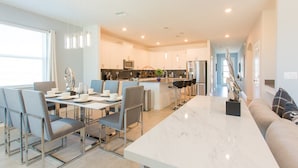 A modern kitchen with stainless steel appliances, a dining area with a marble table, and a living area with a sofa and a decorative sculpture.