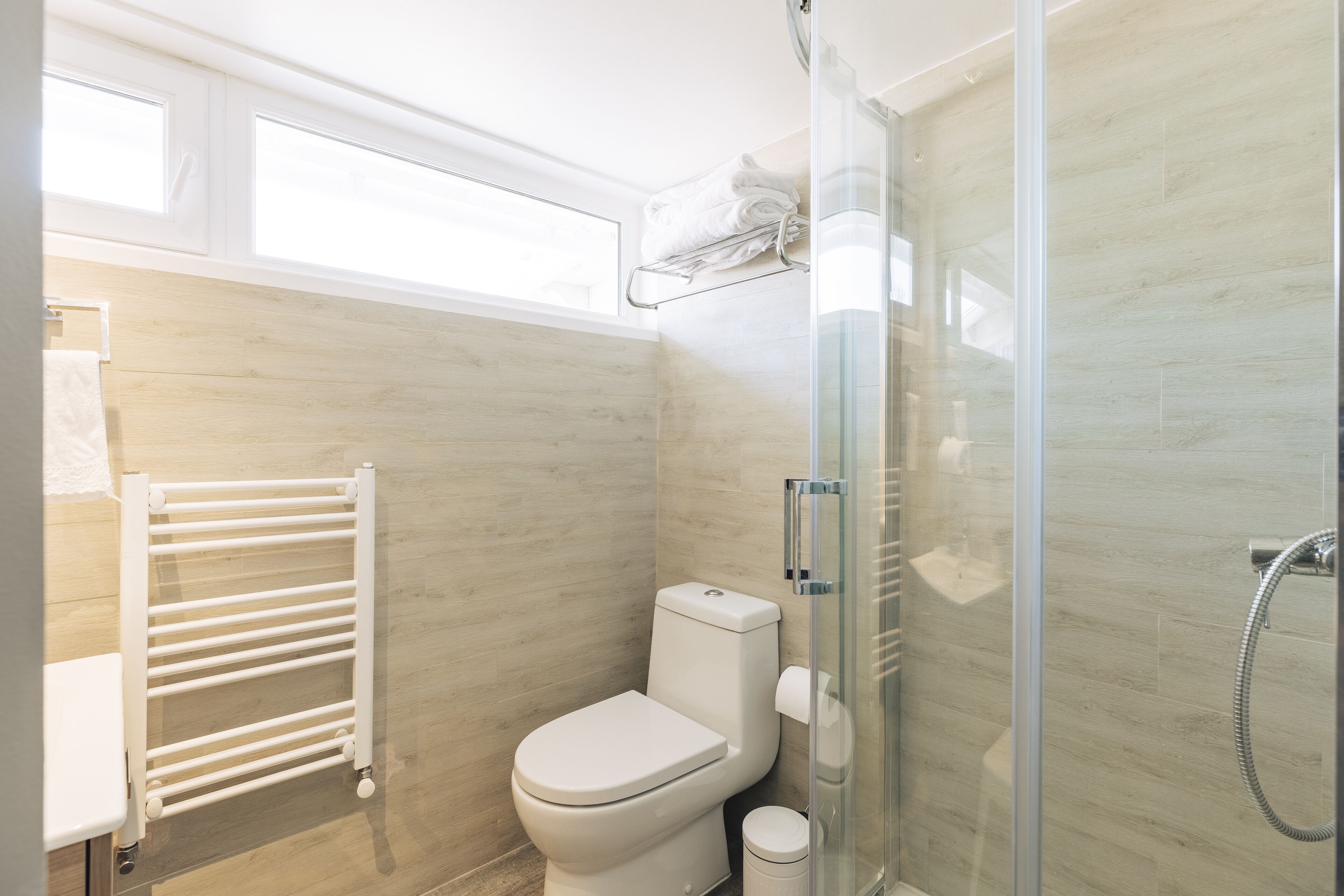 Un baño moderno con cabina de ducha de vidrio, inodoro blanco y un perchero para toallas.