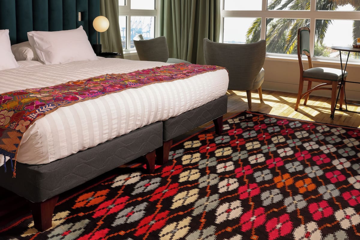 Habitación de hotel con una cama grande, un escritorio y vista a palmeras a través de la ventana.