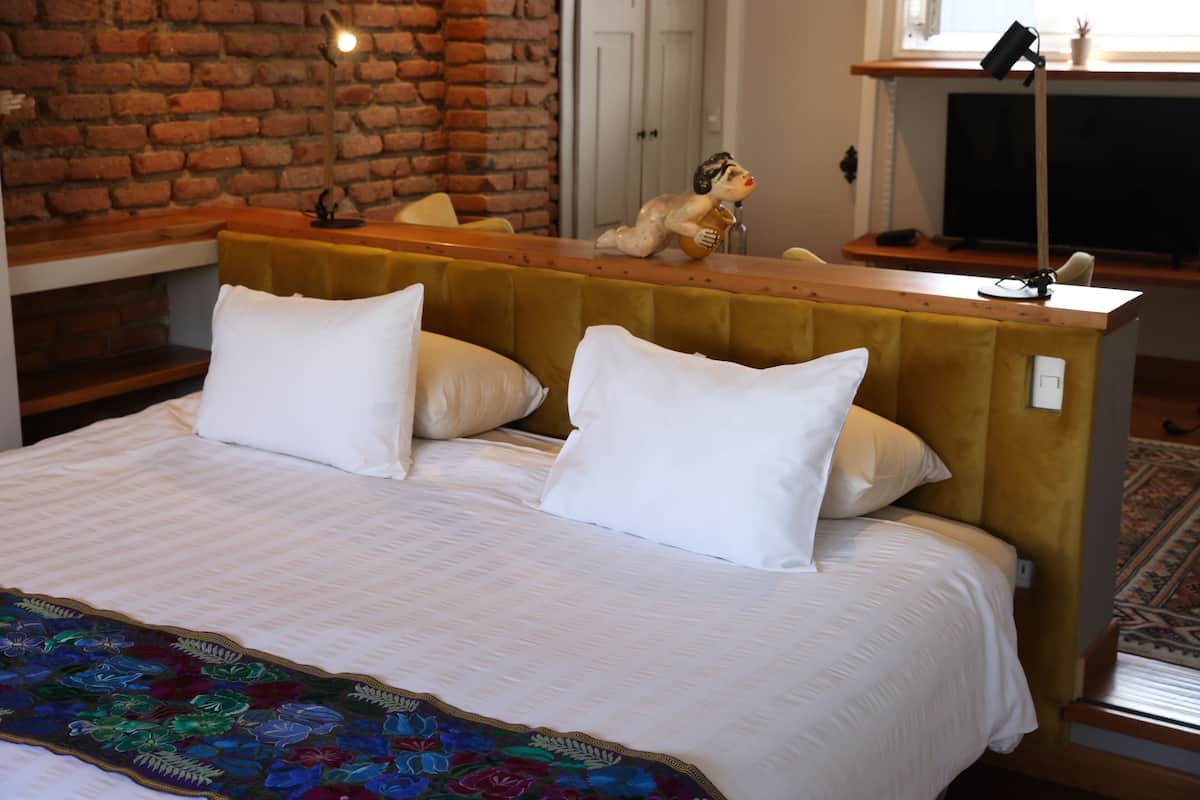 Una cama con ropa de cama blanca, cabecera de madera y una manta bordada de colores.