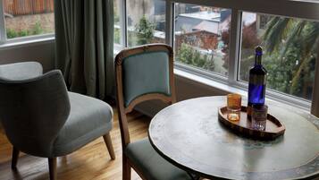 Una habitación con un ventanal grande, una mesa redonda con una botella y vasos, una silla y una alfombra.